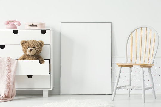 Poster with mockup between chair and cabinet with teddy bear in kid's room interior. Real photo