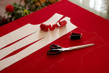 Sewing clothes using a paper pattern. Red fabric, tailor's scissors isantimetric tape for sewing clothes. Draw the base of the dress on the fabric.