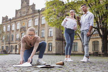 Dropping notebooks. Blonde-haired student in glasses feeling awful while dropping plenty of her...