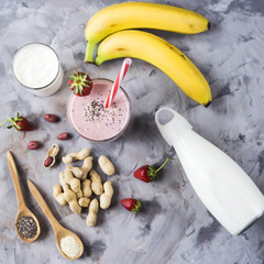 A glass of strawberry banana smoothie among the ingredients for its cooking - strawberries, bananas, milk, yogurt, chia seeds, sesame and peanuts. Healthy eating breakfast. Top view, flat lay