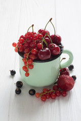Different kinds of berries in enamel tea cup on a white wooden table