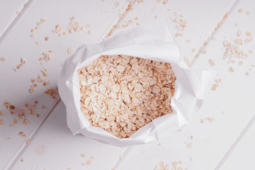 overhead view of bag of rolled oats oatmeal oat flakes on rustic white wooden table
