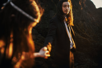 Golden evening sun makes halo around bride and groom while they stand together on the rocks