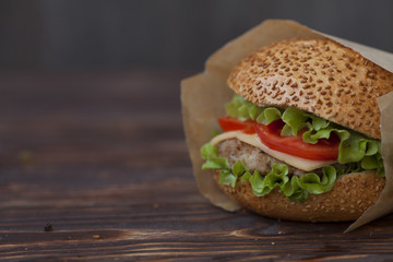 Close-up of delicious fresh home made burger with lettuce, cheese, onion and tomato on a rustic wooden plank on a dark background
