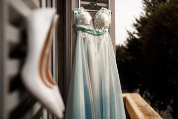 Fototapeta na wymiar White shoes and wedding dress hang on the open window