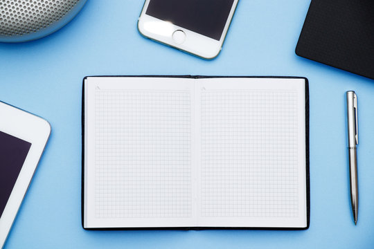 Overhead of office table with laptop, tablet pc, cellphone, speaker and big copy space notebook blue flat lay