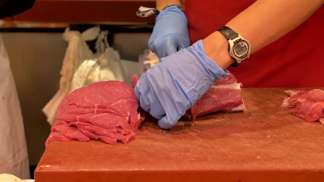 Butcher slicing thin cuts of meat from main cut at a local deli.