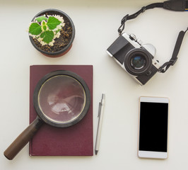 Smart phone magnifying glass on the burgundy notepad and photo camera