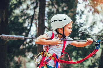 Little boy climbing in adventure activity park with helmet and safety equipment