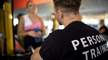 Personal trainer talking to female gym client after workout, sport club service