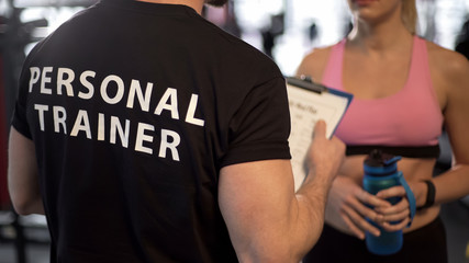 Fitness coach explaining training program and schedule to female client in gym