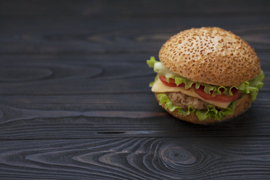Burger with grilled beef, salad, cheese and tomato on dark background. Fast food. Craft burger on wooden background