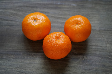 three whole clementines or mandarin oranges on rustic wooden table with shallow depth of field