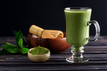 Matcha green tea latte beverage in glass cup on dark wooden background