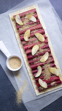 An oblong rhubarb and apple tart sprinkled with sugar on baking paper.