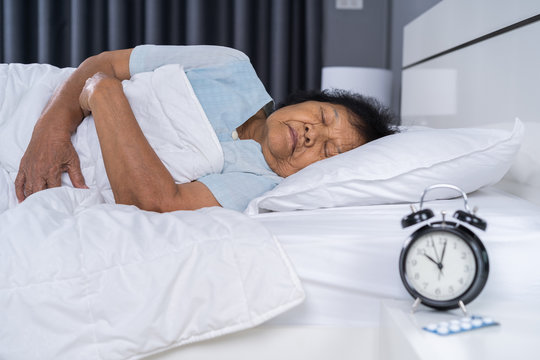 senior woman sleeping on a bed with clock