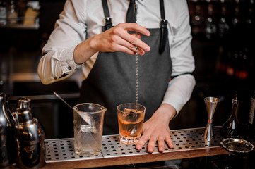 Fototapeta na wymiar Bartender stirring a fresh cocktail in the ornate glass on the bar counter