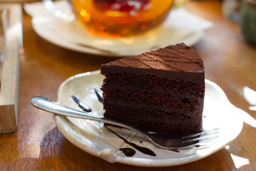 A piece of dark chocolate cake with a fork and tea