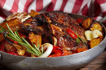 Fried ribs in a pan with rosemary, potatoes rustic, onion, sauce . Dark background.