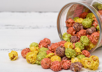 Colored caramel popcorn scattered on a white wooden background