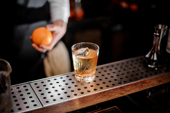 Bartender holding the orange near the fresh alcoholic drink