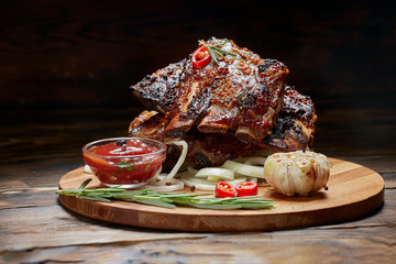 Fried ribs with rosemary, onion, sauce on a wooden round Board. Dark background. Place for text, copyspace