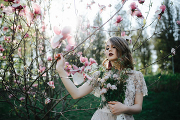 very beautiful girl the bride under a veil, beige wedding dress near the tree Sakura is looking...