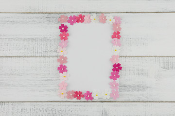 Blank white card decorate with pink paper flowers on white wood background
