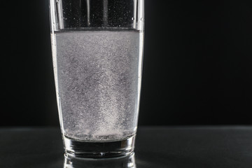Glass with efervescent tablet in water with bubbles isolated on white