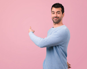 Handsome man pointing back with the index finger on pink background