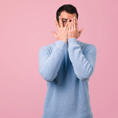 Handsome man covering eyes by hands on pink background