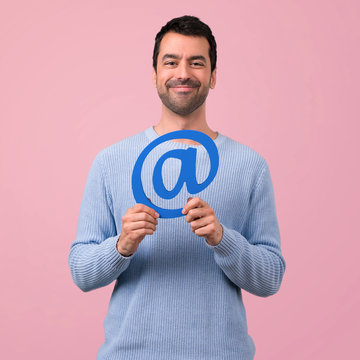 Man with blue sweater holding icon of at dot com on pink background