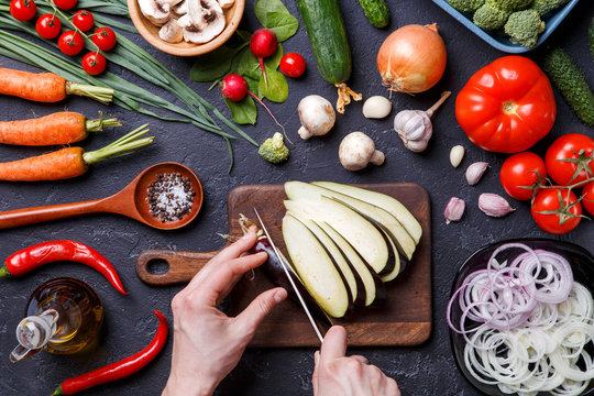 Image on top of fresh vegetables, champignons, cutting board, oil, knife, eggplant, chef's hands