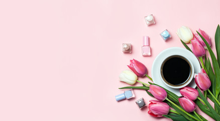 Cup of coffee, pink tulips and nail pilishes on pink background.