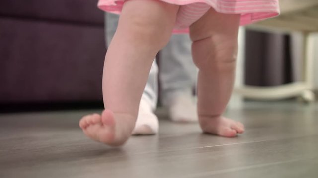 Little baby learning walk on floor. Cute baby feet learn to walk with daddy. Toddler walking at home. Infant doing first steps with father. Little feet learning going. Sweet child care