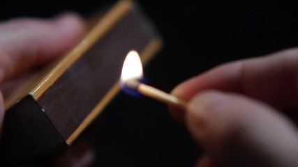 Close up of hands lighting a match.
