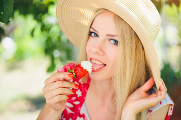 young blond woman eating strawberries with cream, happy in the garden on a summer sunny day, warm summer tonic image, self-service and healthy lifestyle