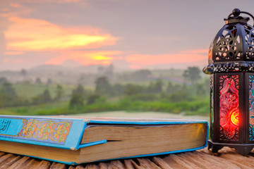 Quran, and lantern on old wood with a beautiful sunrise as background. Ramadhan Concept.