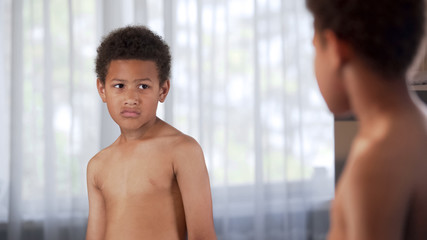 Fototapeta na wymiar Unhappy little African American boy looking in mirror, suffering insecurities