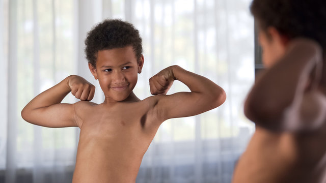Confident kid looking at his muscles in mirror imagining that he is super hero