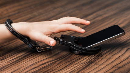 The smartphone is handcuffed in the hand of a little boy. a symbol of abuse of technology. High...