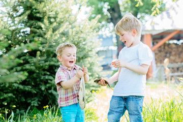 Fototapeta premium High emotions shot of two excited blond brothers little fishmen enjoying the catch, holding fishes in hands in sunny summer day outdoor. Childhood, friendship and adventure concept.
