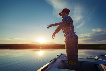 Man fishing in a pond from a boat at sunset