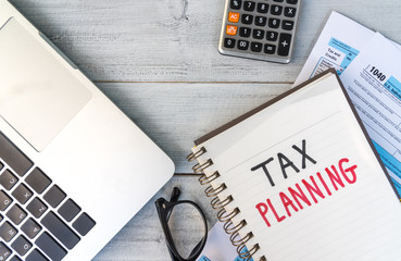 Tax planning hand written in a note with tablet, calculator, eyeglasses and tax return form on desk.