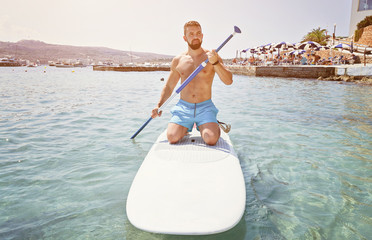 Adult bearded man beginner surfer kneel on paddle board on sea. Summer active vacation and water sport concept © Kira_Yan