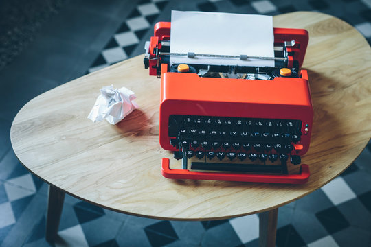 Red typewriter and crumpled paper on small table