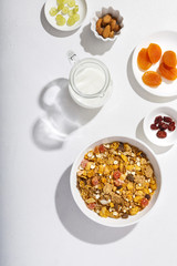 Muesli served with milk, honey, almonds, dried apricots and dried cranberries. Vertical shot. Flatlay.