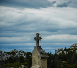 Tombstone with cross at old cemetery and rocky mountains at background (Provence, France).