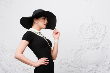 Portrait of a beautiful young woman in retro style in an elegant black hat and dress over luxury...