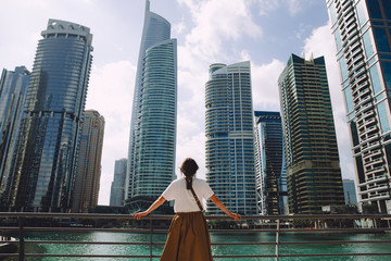 Fototapeta na wymiar Female traveler looking at modern city architecture against blue sky, Dubai, UAE